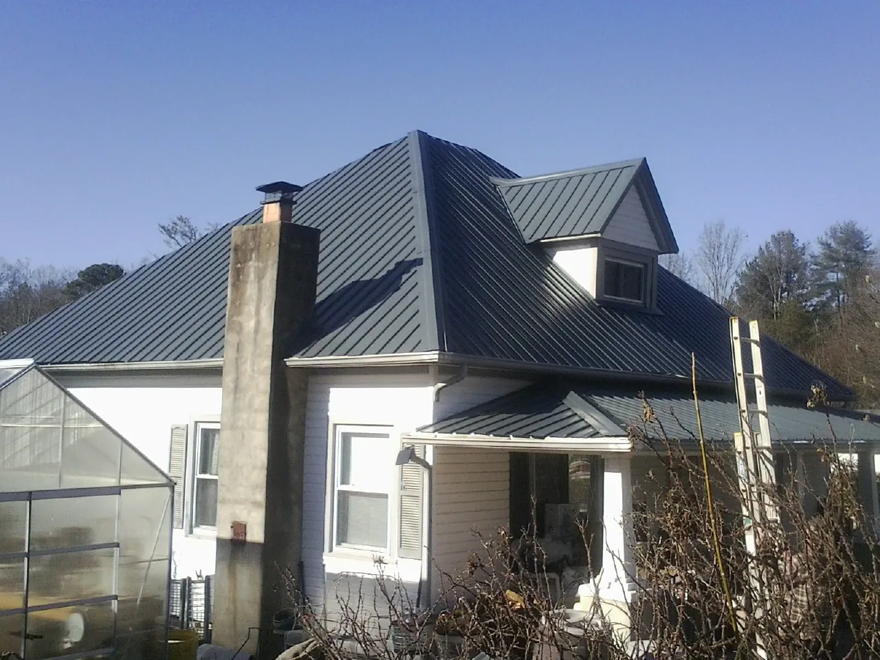 Dark blue standing seam metal roof on a white farmhouse with dormer — Slate & Tile Roof Repair by Roofing Brothers in Terreton