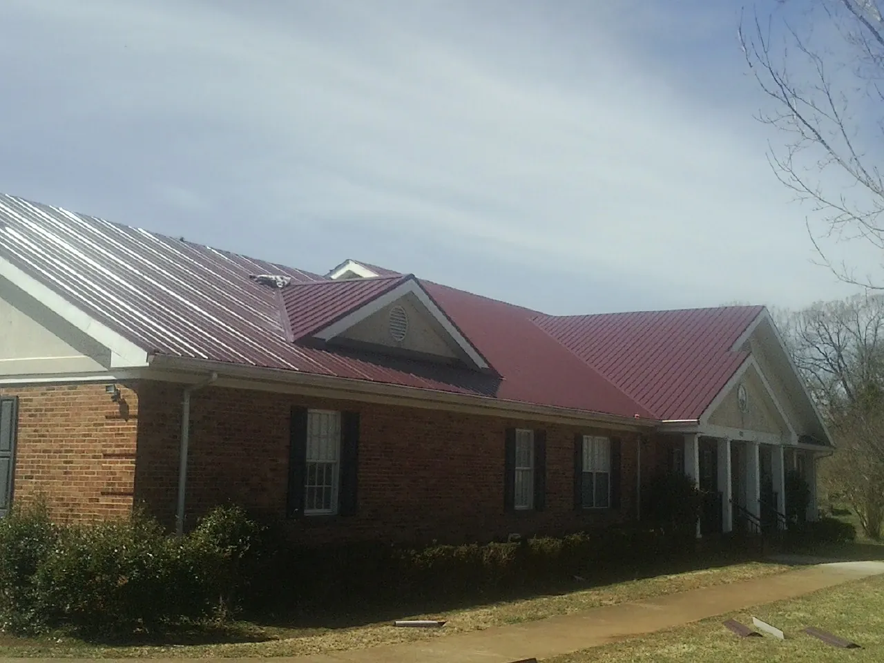 Red metal roof with gabled entries on a long brick building, from a Hail Damage Roof Repair job in Terreton