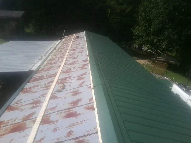 Old rusted panels beside newly installed green metal roofing — Wind Damage Roof Repair by Roofing Brothers in Terreton