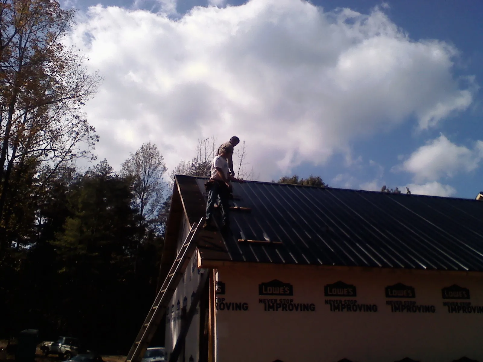 Roofer fastening dark metal panels high against a cloudy sky, from a Roof Inspection job in Terreton