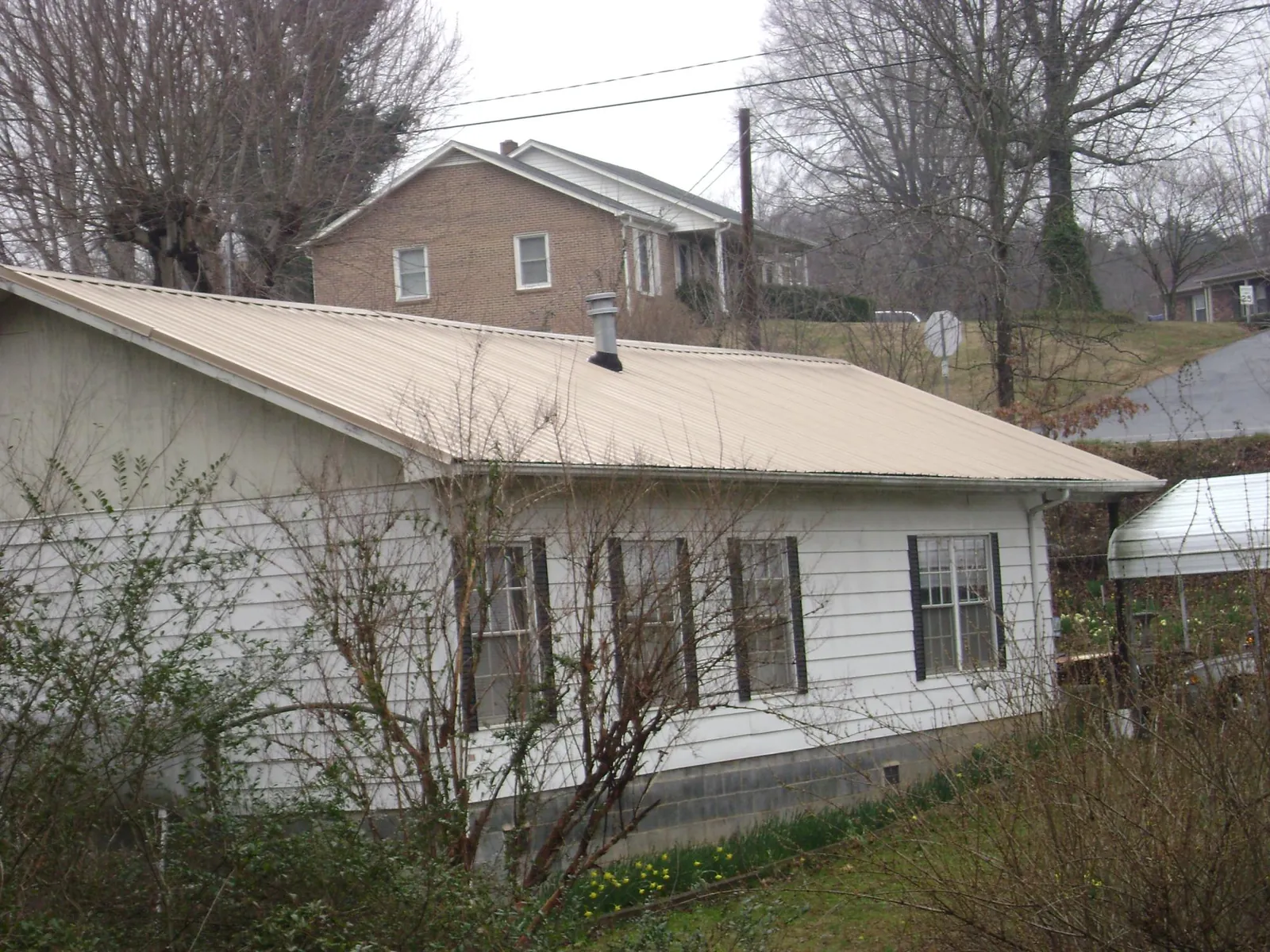 Tan metal roof on a white sided house set into a hillside — Commercial Roofing by Roofing Brothers in Terreton